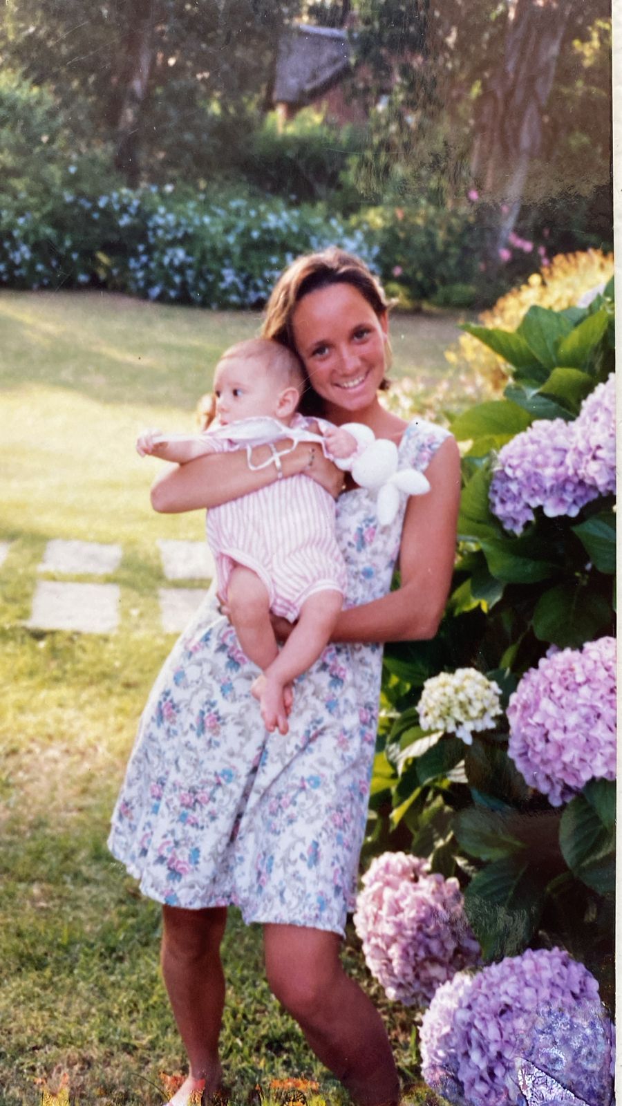 Woman holding a baby in a garden with hydrangeas