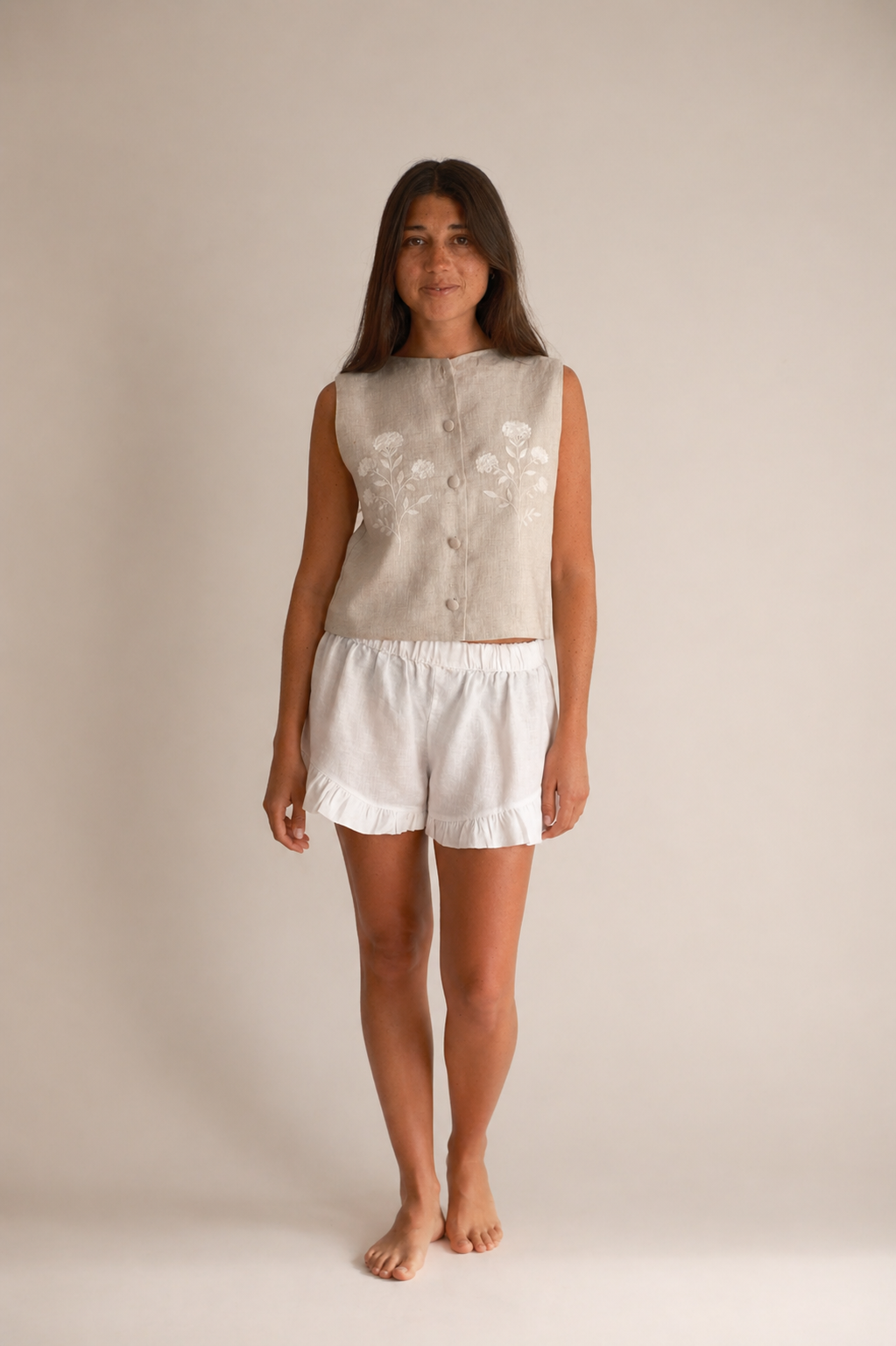 Woman wearing a beige sleeveless top and white shorts on a plain background