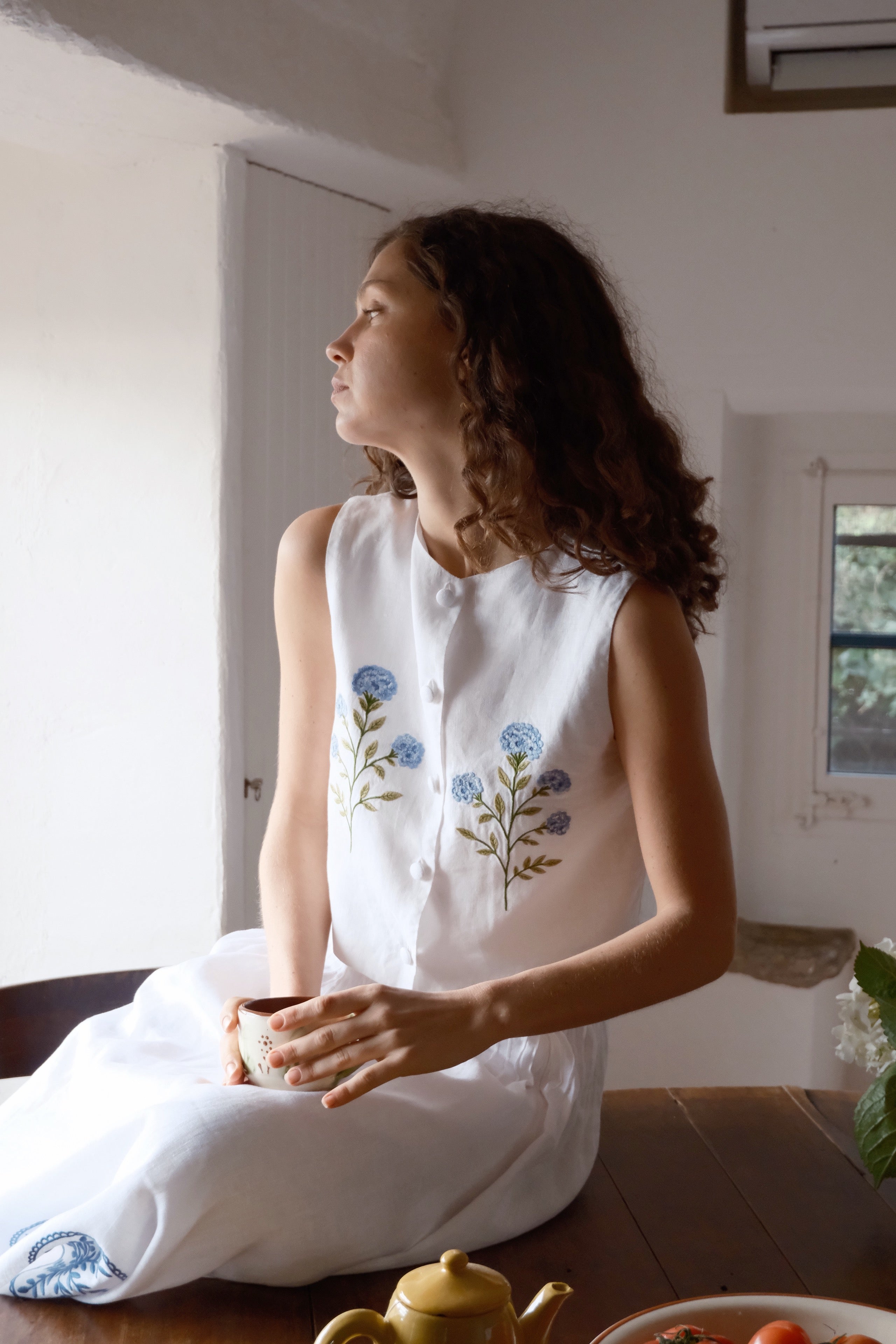 Woman wearing a white sleeveless top with floral embroidery in mediterranean house