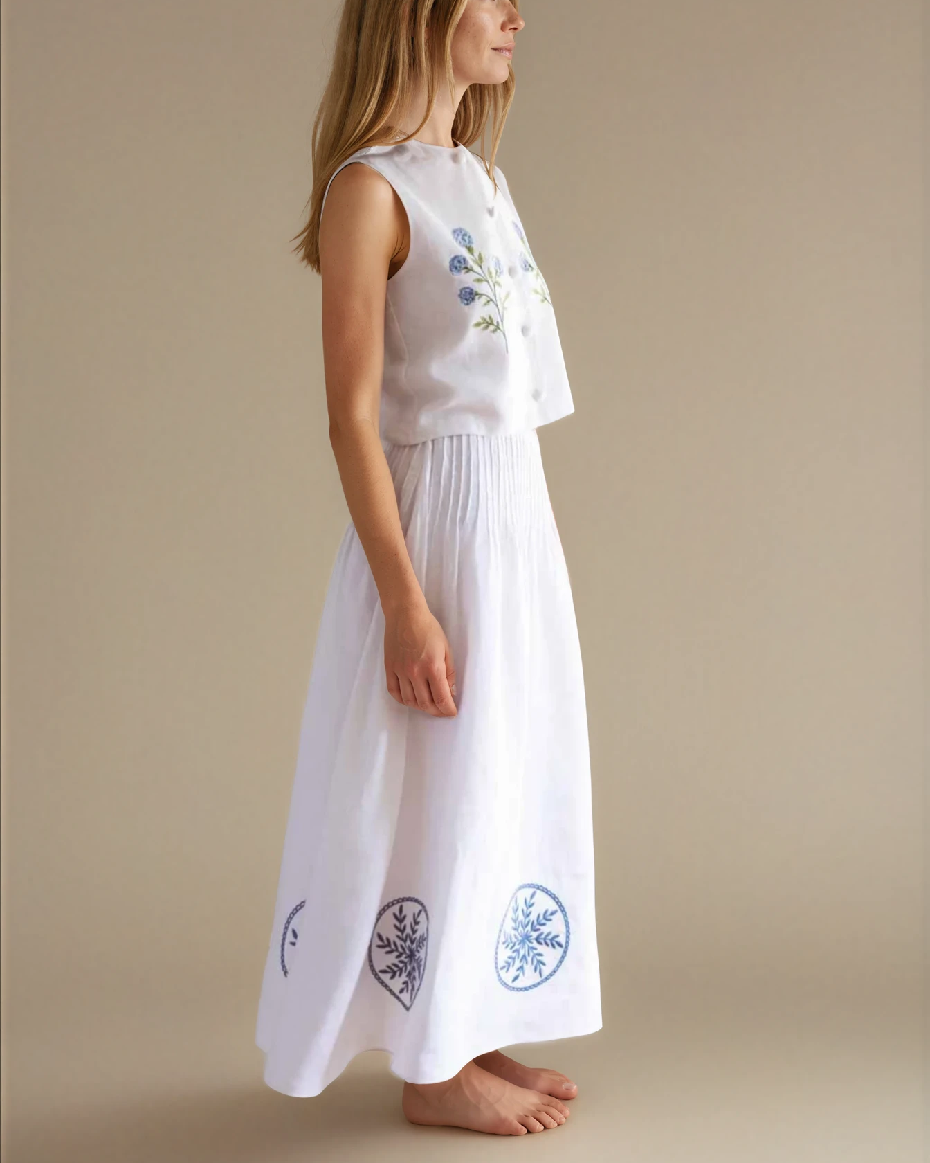 Woman wearing a white sleeveless top and long white skirt with blue embroidery