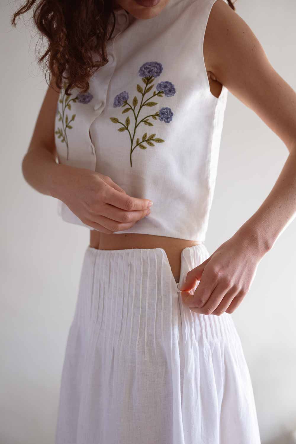 Woman wearing a white sleeveless top with floral embroidery and white skirt 